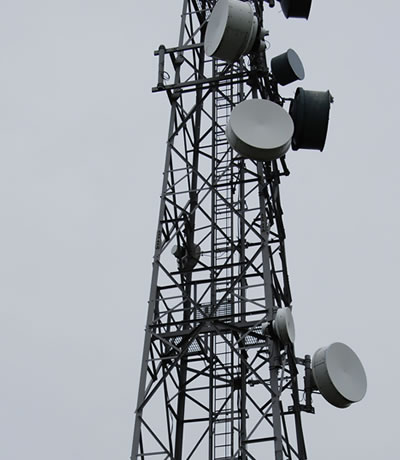 Telecommunications tower with multiple microwave and radio antennas against a grey sky.